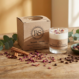 Glass candle with decorative elements on a wooden surface, featuring 'Beauty Scents' branding.