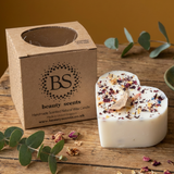 Beauty Scents Large Heart Candle With Rose Petals next to its branded box on a wooden table 