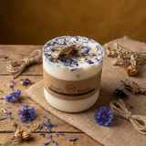 Candle with dried flowers on a wooden surface, surrounded by more flowers.