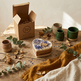 Heart-shaped candle with dried flowers on a wooden surface with ceramic containers and eucalyptus leaves.