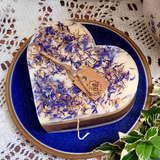 Heart-shaped candle with dried flowers on a blue plate with a plant and lace background