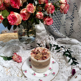 Medium handmade rose petal candle on vintage floral plate, with fresh pink roses in vase, lace tablecloth background