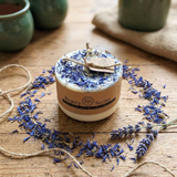 Small handmade wild flower candle with kraft label, decorated with dried blue petals, on rustic wooden table