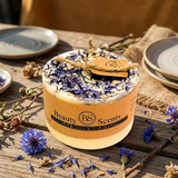 Candle with decorative packaging on a wooden surface with flowers
