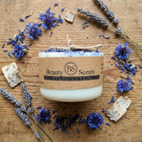 Candle with wildflowers on a wooden surface, featuring 'Beauty Scents' branding.
