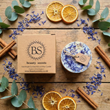 Small handmade wild flower candle with kraft label and dried blue petals, Beauty Scents gift box, dried orange slices, cinnamon sticks, eucalyptus on rustic wooden table
