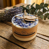Small handmade wild flower candle with kraft label, decorated with dried blue petals, lavender and eucalyptus on rustic wooden table
