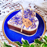 Decorative candle with dried flowers on a blue plate, surrounded by green leaves.