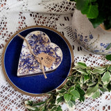 Decorative heart-shaped candle with a tag on a blue plate, surrounded by greenery and lace fabric.